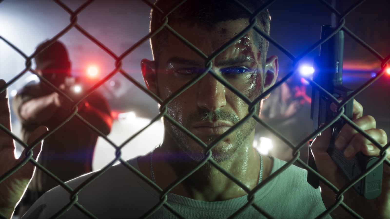Jason looks through a chain-link fence with police lights behind him in an official GTA VI screenshot.